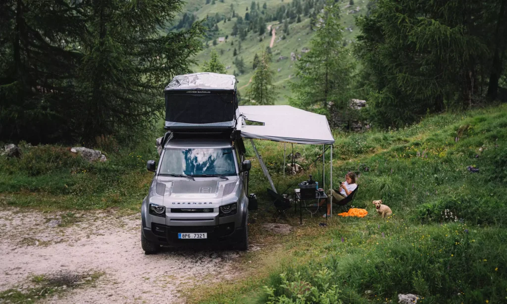 Katerina Hrnová Sitting with Dog in a Green Landscape under a Falcon Awning 270 and an Open Rooftop Tent, Setup on Car