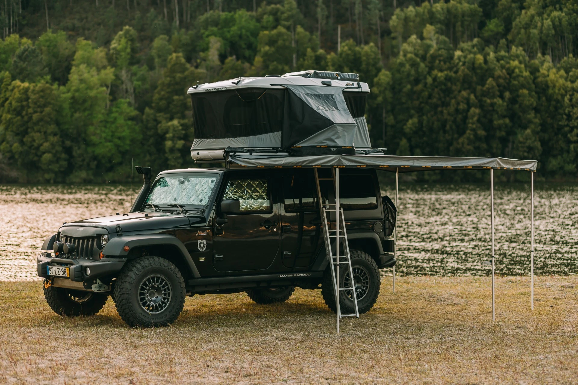 A car wiht a ground support awning parked in grass and water by the side