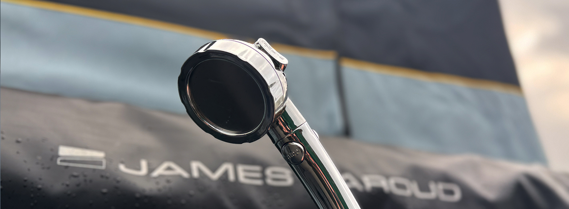 Close-up of a camping showerhead, set against a blurred background featuring a James Baroud rooftop