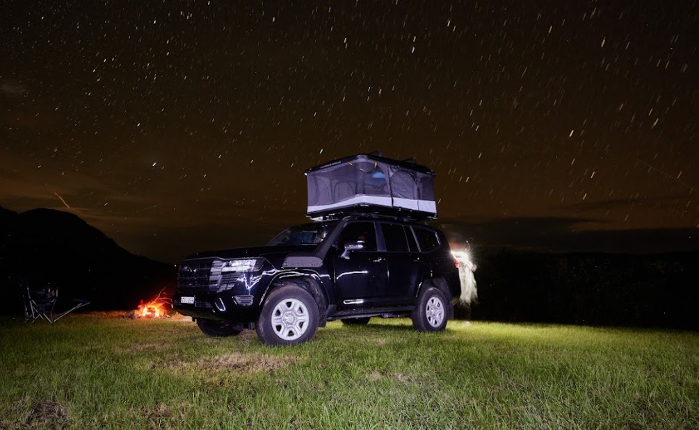 A car with a rooftop tent and acar awning parked by the lake