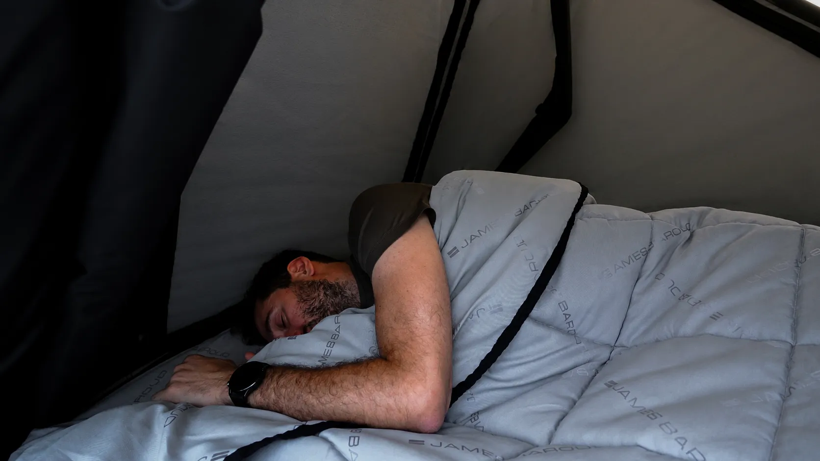 Person sleeping inside a rooftop tent using the James Baroud TBS bedding system